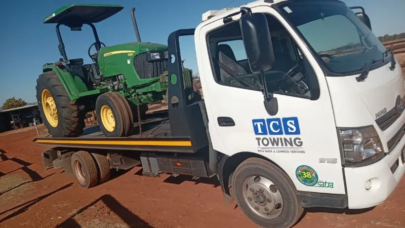 Flatbed truck transporting green tractor
